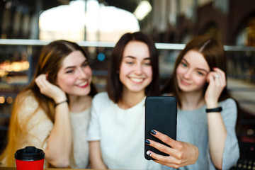 Three friends make selfie and drink coffee at cafe