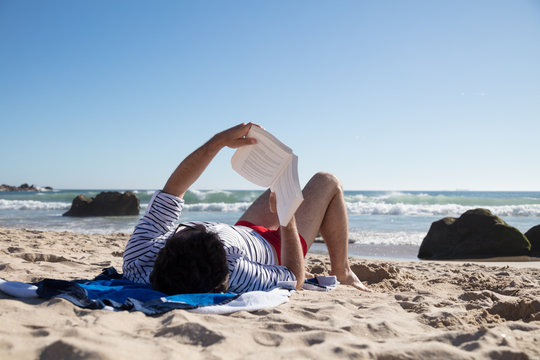 Rear view of man at the beach and reading book