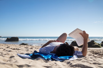 Man reading a book while lying on towel