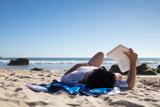 Man reading a book while lying on towel