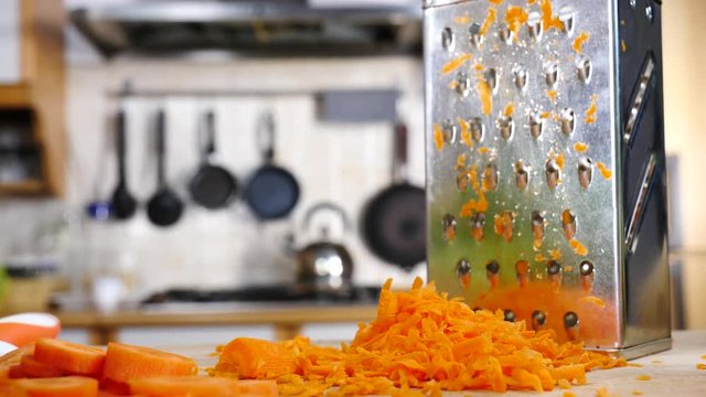 Close up of grate and sliced chopped carrot on kitchen board in slow motion."