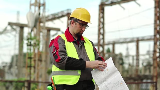 Worker with scheme of works on power station. Power man with construction documentation at power plant. Master builder in hard hat with design drawings