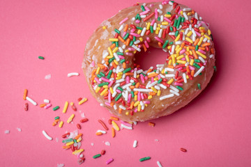 Top view of  glazed doughnut with colorful sprinkles on a pink background.