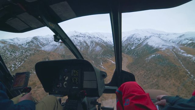 Inside view of a helicopter in flight, with man and pilots flying over the mountains