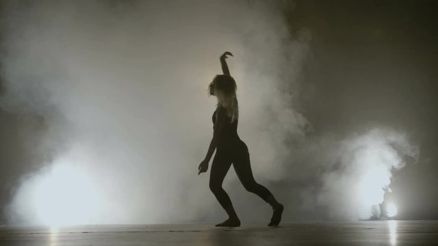 Young fit girl dancing on a smoke background while recording a music video clip for a famous singer