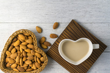almonds milk with almonds in heart shape basket on white wooden