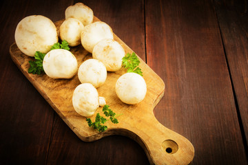 Champignon with greens on cutting board on wooden background
