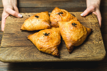 Uzbek national dish of samsa on a wooden board in the hands of a girl