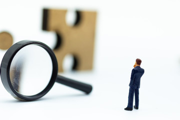 Miniature people : Businessman looking at jigsaw pieces through a magnifying glass. Image use for solve, solution, business concept.