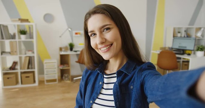 POV. Close up of the brunette attractive woman smiling in the camera while doing selfie in the urban office room. Portrait. Inside