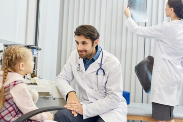 Obraz premium Male doctor talking with little patient while his colleague working in the background