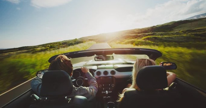 Couple driving into the sunset in convertible