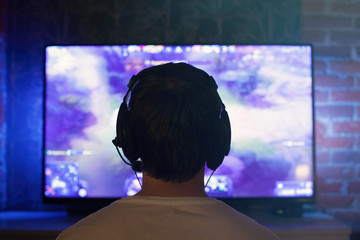 Gamer or streamer in earphones with microphone sits at home in dark room and plays with friends on networks in video games. A young man sits in front of a monitor or TV © Vasiliy