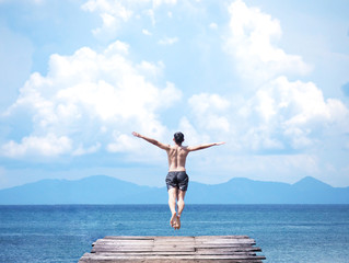 Fototapeta na wymiar man jumping off wooden bridge into blue sea.