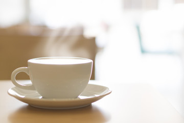 Closeup hot coffee cup with smoke and light from out door for holiday or relax concept, selective and soft focus