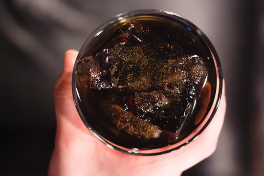 Whiskey or cola with ice. Stakan in the male hand is a top view. Dark background.