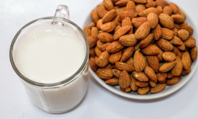 Almond milk in glass with almonds on white background