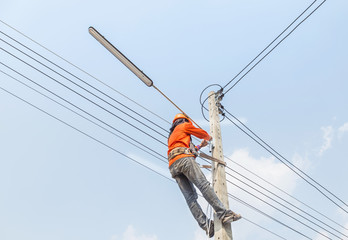 Electrician climb work installing new street lamp on electricity power concrete pole in blue sky    