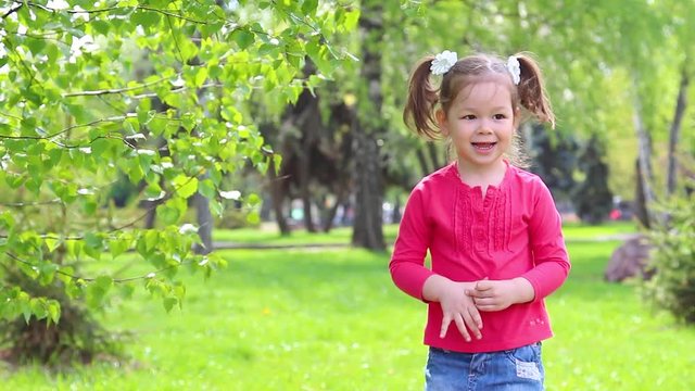Cute little funny girl playing outdoors happily. Child jumping on green grass lawn in park.