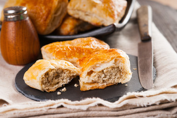 Pie made from puff pastry with meat on plate, salt shaker and knife