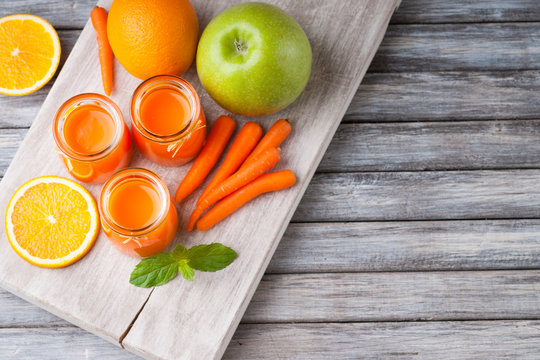 Jars with carrot juice, apple, sliced orange and mint leaf 