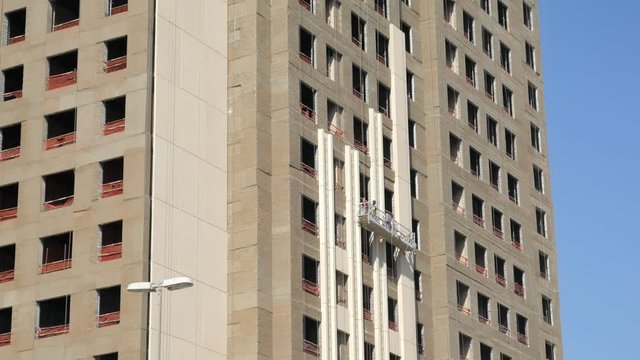 high-rise builders are working in a suspended cradle on a facade of building