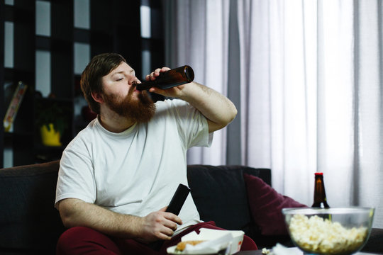 Fat man drinks beer lying on the sofa