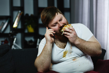 Ugly fat man talks on his smarphone while he eats a burger
