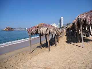 Scenery of exotic bamboo huts on sandy beach at bay of ACAPULCO city in Mexico with skycraper and...