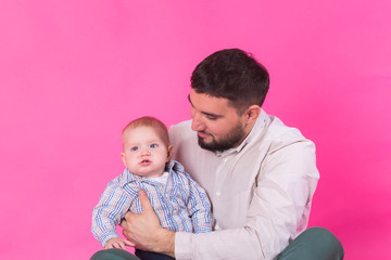 Happy portrait of the father and son on pink background. In studio