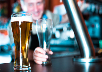 glass of beer on bar counter against background of friendly bartender