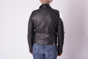 Fashionable man in leather jacket is standing on grey background