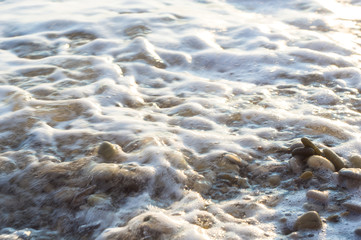 pebble stones on the sea beach, the rolling waves of the sea with foam