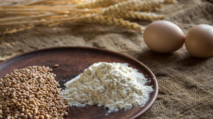 wheat flour eggs and spikelets of wheat on sackcloth background