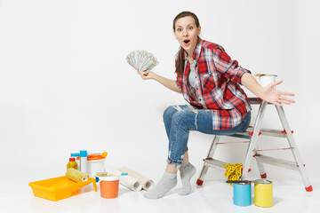 Woman holds bundle of dollars, cash money, sits on ladder with instruments for renovation apartment...