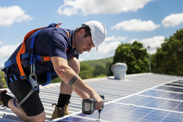 Solar panel technician with drill installing solar panels