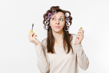 Fun young woman with curlers painting eyelashes with mascara isolated on white background. Crazy...