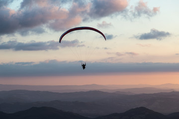 Beautiful shot of a paraglider silhouette flying over Monte Cucco (Umbria, Italy) with sunset on...
