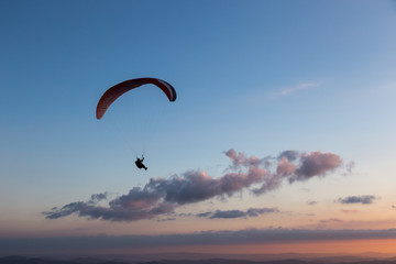 Beautiful shot of a paraglider silhouette flying over Monte Cucco (Umbria, Italy) with sunset on the background, with beautiful colors and dark tones