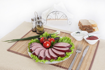 Smoked sausage with tomatoes and lettuce leaves on a plate.