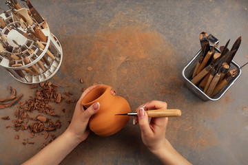 a woman holding a vase of clay in a pottery workshop. a vase of clay in the hands of the master and tools on the table top view. potter top view . copyspace