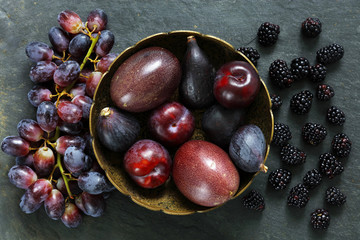 Dark Exotic Fruits on slate background including passion fruit, plums, figs, grapes, black berries