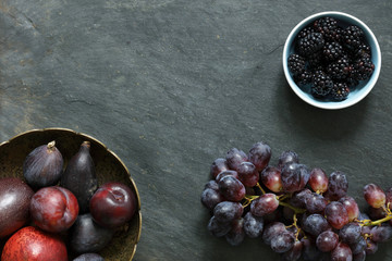 Dark Exotic Fruits on slate background including passion fruit, plums, figs, grapes, black berries, with copy space
