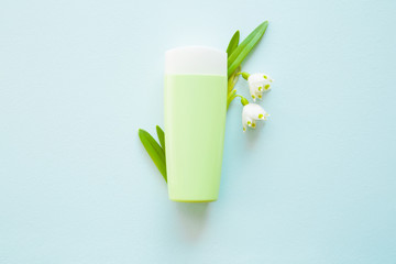 Green bottle of natural herbal cream for women on the pastel blue background. Beautiful, fresh snowdrop flowers. Care about clean and soft hands, legs and body skin. Top view. Beauty concept.