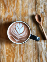 Hot chocolate latte art heart shape in white and black cup and wooden spoon on vintage wooden table.vintage style and natural light