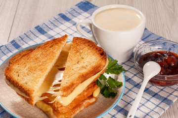 Toasted slices of bread with cheese and green parsley on white plate, cup of coffee, bowl with strawberry jam and spoon on napkin
