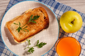 Toast with butter and cheese on white plate, apple and glass of orange juice