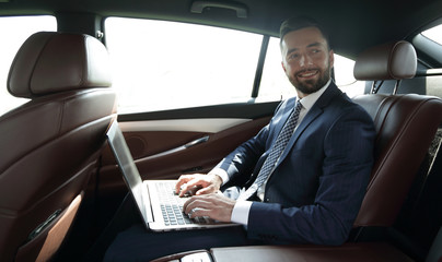 businessman with laptop sitting in the back seat of a car