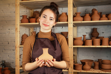 a young and cheerful woman holding a vase of clay. The potter works in a pottery workshop with clay. the concept of pottery mastery and creativity