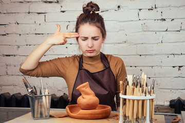 The concept of sadness and lack of ideas in creativity. A young and sad woman looks at a vase of clay. The potter makes a vase at the table in a pottery workshop.